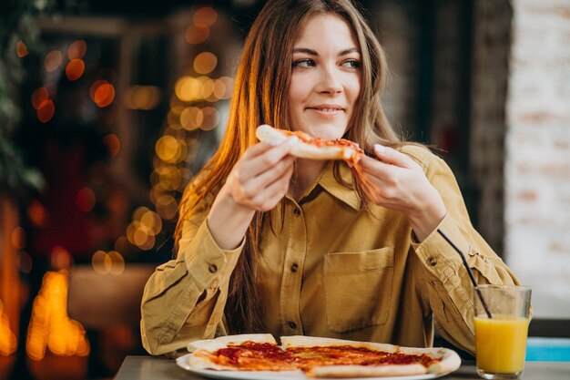 Jeune jolie femme mangeant de la pizza dans un bar