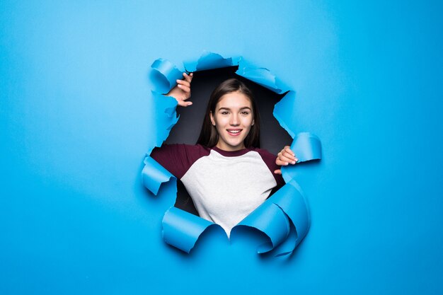 Jeune jolie femme regardant à travers le trou bleu dans le mur de papier.