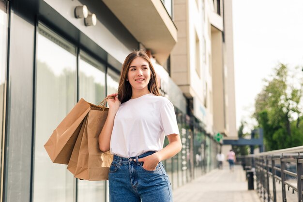 Jeune jolie femme avec des sacs à provisions marchant sur la rue de la ville