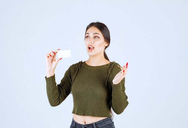 Jeune jolie femme tenant une carte de visite vierge avec une expression surprise.