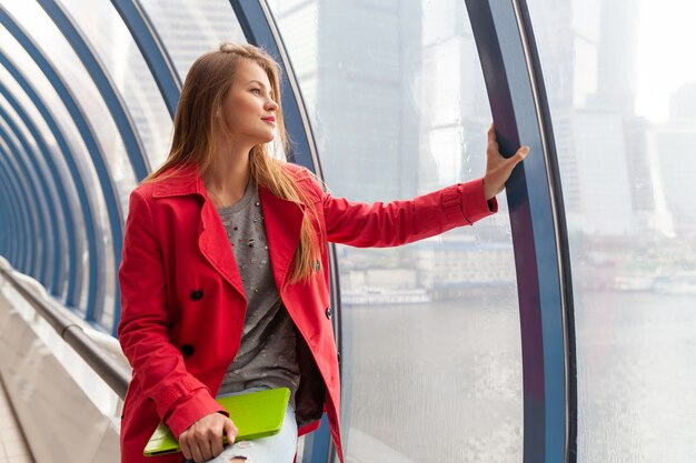 Jeune jolie femme en tenue décontractée tenant un ordinateur portable tablette dans un bâtiment urbain