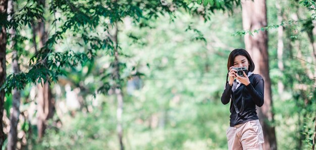 Jeune jolie femme utilise un appareil photo numérique en prenant une photo de la belle nature en camping dans la forêt avec un espace de copie de bonheur