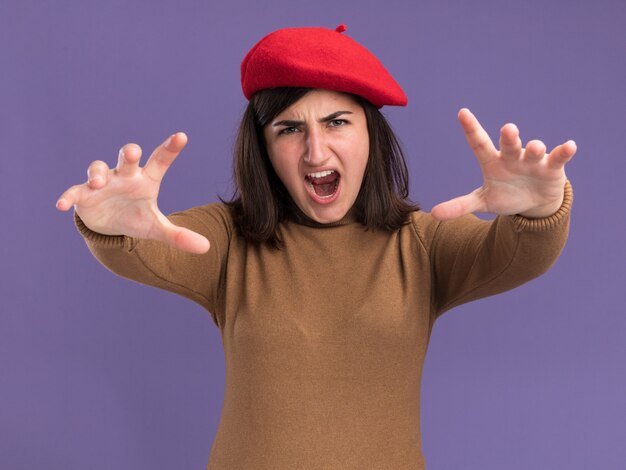 Photo gratuite jeune jolie fille caucasienne agacée avec un chapeau de béret tendant les mains isolées sur un mur violet avec espace de copie