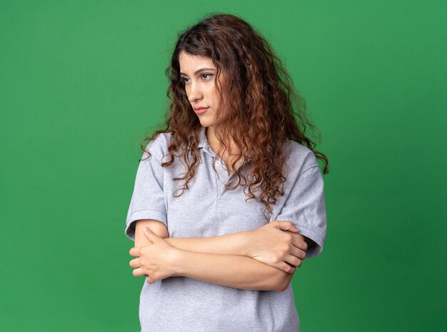 Jeune jolie fille caucasienne debout avec une posture fermée regardant le côté isolé sur un mur vert avec espace de copie