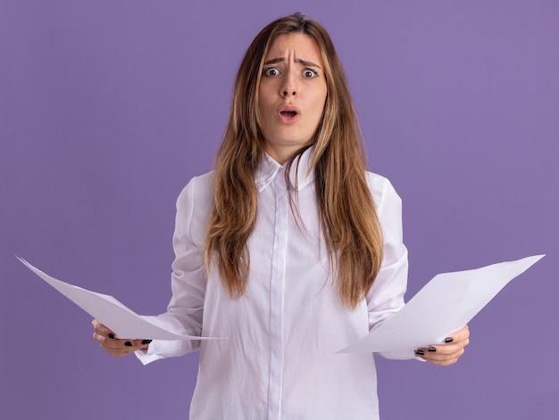 Une jeune jolie fille caucasienne inquiète tient des feuilles de papier