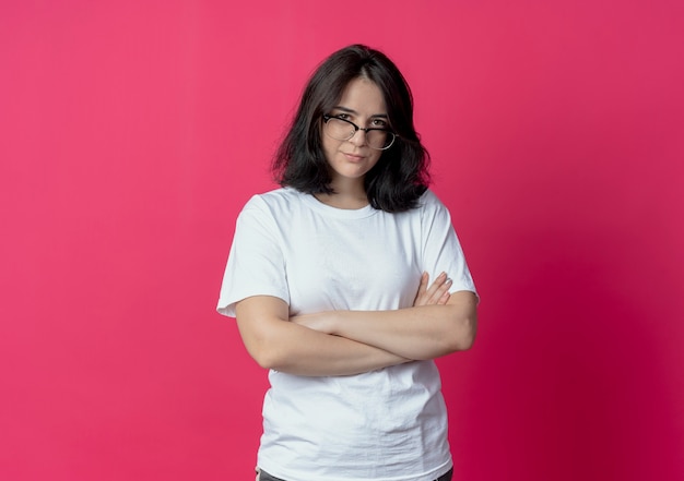 Jeune jolie fille caucasienne portant des lunettes debout avec une posture fermée et regardant la caméra isolée sur fond cramoisi avec espace copie