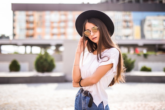 Jeune jolie fille avec chapeau noir et lunettes de soleil à l'extérieur sur la rue ensoleillée