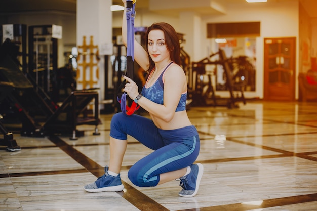 Jeune et jolie fille dans un costume de sport bleu est engagée dans les sports dans la salle de gym