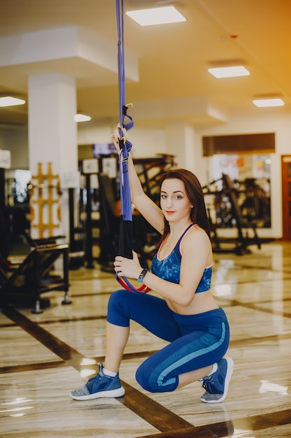 Jeune et jolie fille dans un costume de sport bleu est engagée dans les sports dans la salle de gym