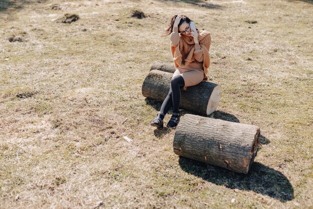 Jeune jolie fille élégante sur la nature sur le mur de la forêt avec téléphone par une journée ensoleillée. vacances en plein air et dépendance à la technologie.