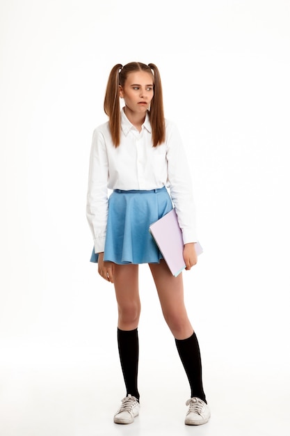Jeune jolie fille émotionnelle en uniforme posant sur mur blanc