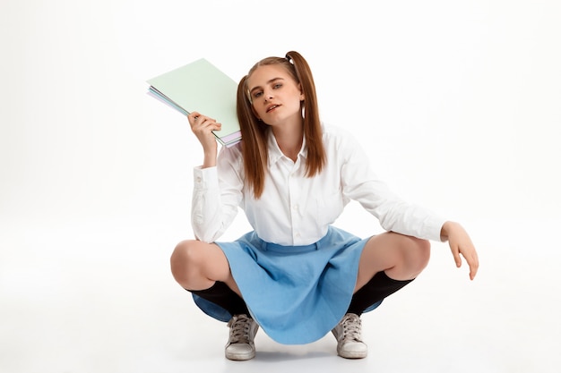 Jeune jolie fille émotionnelle en uniforme posant sur mur blanc