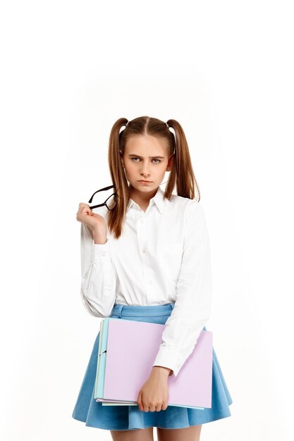Jeune jolie fille émotionnelle en uniforme posant, tenant des papiers, isolée sur blanc