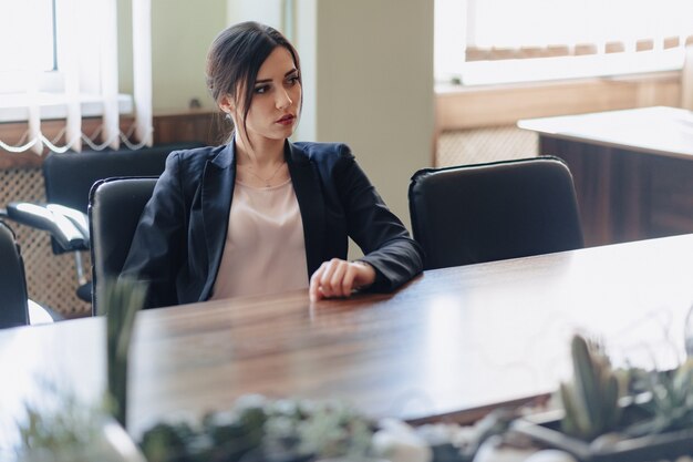 Jeune jolie fille émotionnelle en vêtements de style professionnel assis au bureau avec téléphone au bureau ou au public