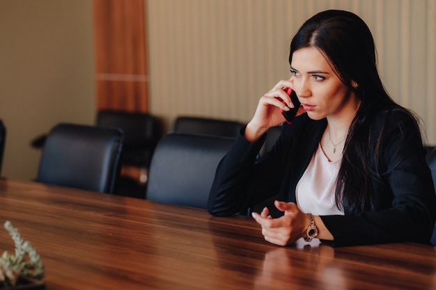 Jeune Jolie Fille émotionnelle En Vêtements De Style Professionnel Assis Au Bureau Avec Téléphone Au Bureau Ou Au Public