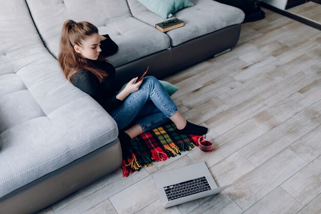 Jeune jolie fille à la maison travaillant avec un ordinateur portable et parlant au téléphone. confort et confort à la maison. bureau à domicile et travail à domicile. emploi à distance en ligne.