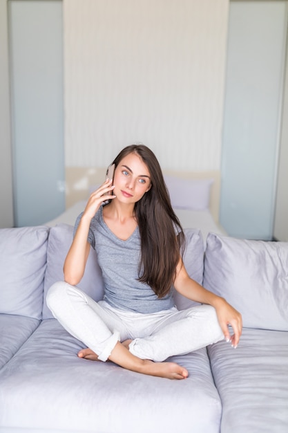 Jeune jolie fille parlant au téléphone sur le canapé à la maison