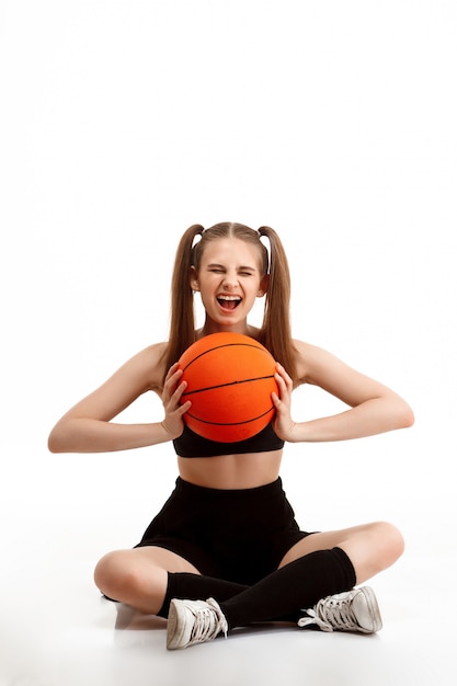 Photo gratuite jeune jolie fille posant avec basket-ball sur mur blanc