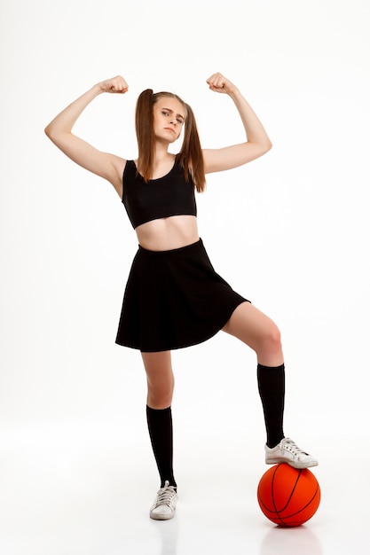 Jeune jolie fille posant avec basket-ball sur mur blanc