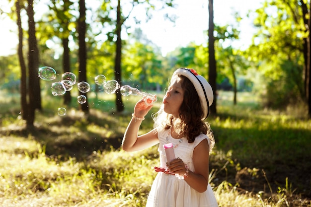 Jeune jolie fille soufflant des bulles, marchant dans le parc au coucher du soleil.