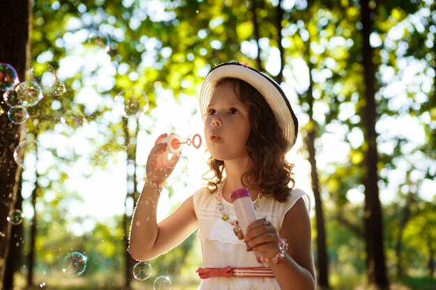 Jeune jolie fille soufflant des bulles, marchant dans le parc au coucher du soleil.