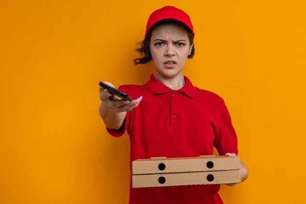 Jeune jolie livreuse agacée tenant des boîtes à pizza et un téléphone