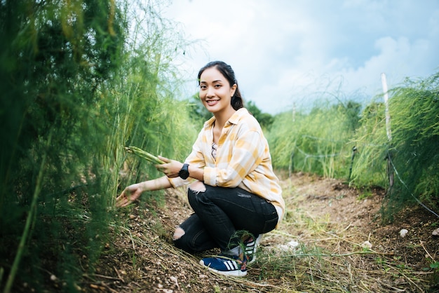 Jeune jolie paysanne récolte des asperges fraîches avec la main dans le champ.
