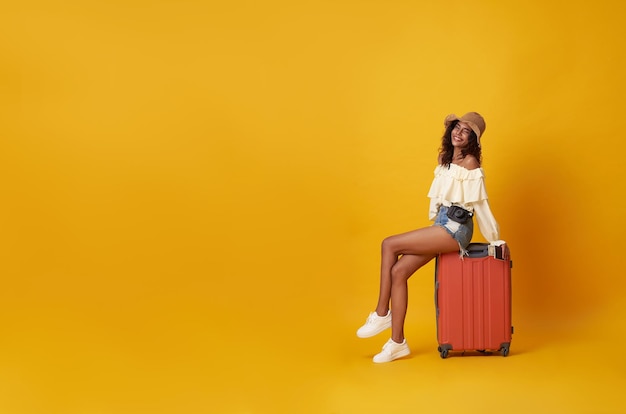 Jeune jolie touriste africaine souriante assise sur des bagages avec caméra à la main