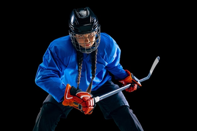 Jeune joueuse de hockey avec le bâton isolé sur fond noir. sportive en action portant un équipement attaquant pour le but ou le score. concept de sport, mode de vie sain, mouvement, mouvement.