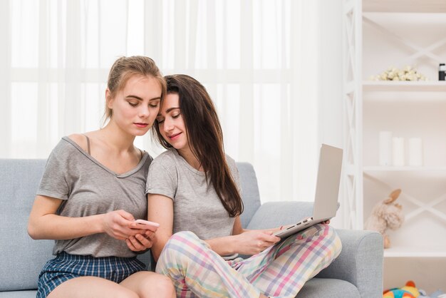 Jeune lesbienne tenant un ordinateur portable sur ses genoux à la recherche dans le portable de sa petite amie