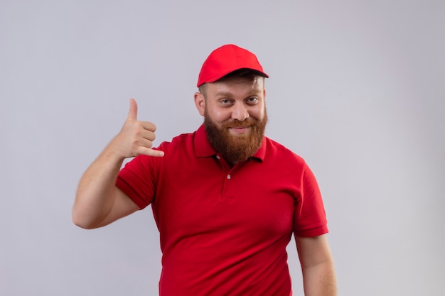 Jeune livreur barbu en uniforme rouge et chapeau souriant faisant cal me geste avec la main