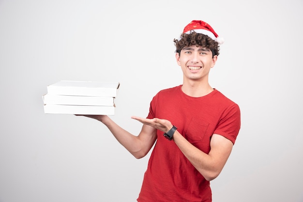 Jeune livreur en bonnet de Noel tenant des boîtes à pizza.