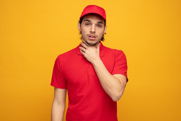 jeune livreur malsain portant l'uniforme et la casquette gardant la main sur le cou regardant la caméra ayant mal à la gorge isolé sur fond jaune