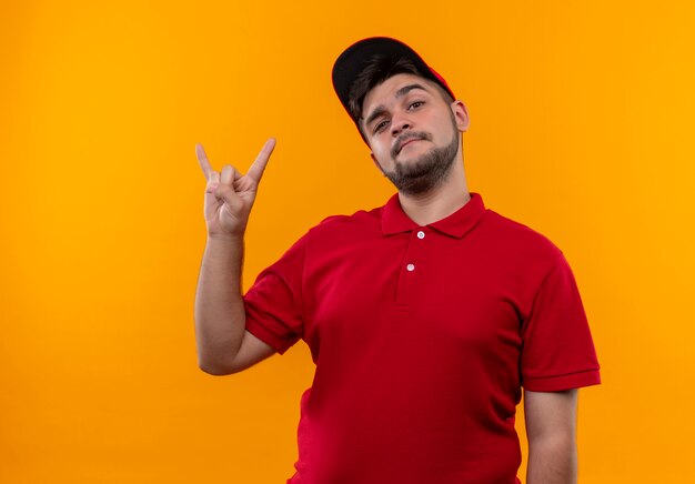 Jeune livreur en uniforme rouge et cap faisant symbole rock avec fingrs à la confiance