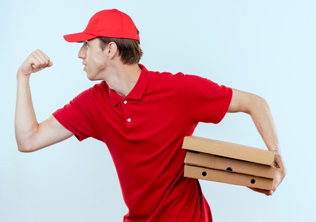 Jeune livreur en uniforme rouge et cap rush en cours d'exécution pour livrer des boîtes de pizza à un client sur un mur blanc