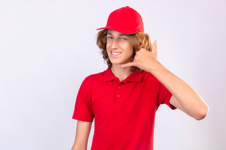 Photo gratuit jeune livreur en uniforme rouge faisant appelez-moi le geste à la confiance souriant joyeusement sur fond blanc isolé