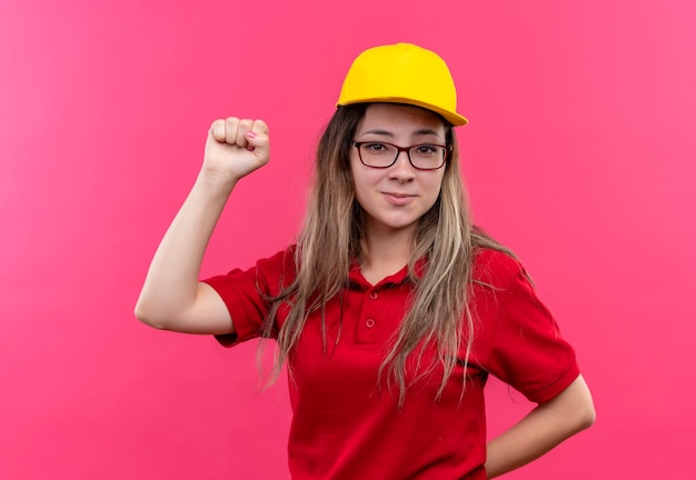 Jeune livreuse en polo rouge et bonnet jaune poing positif et heureux, concept gagnant