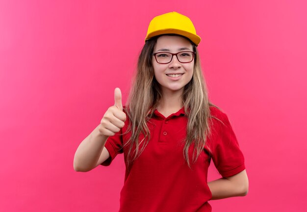 Jeune livreuse en polo rouge et casquette jaune souriant montrant les pouces vers le haut