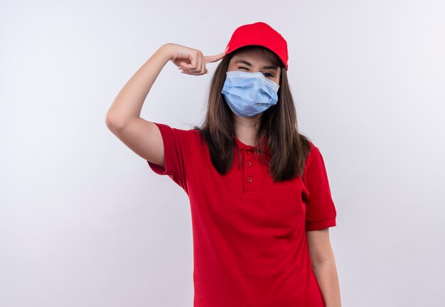 Jeune livreuse portant un t-shirt rouge à bonnet rouge porte un masque facial mettre le doigt sa tête sur fond blanc isolé