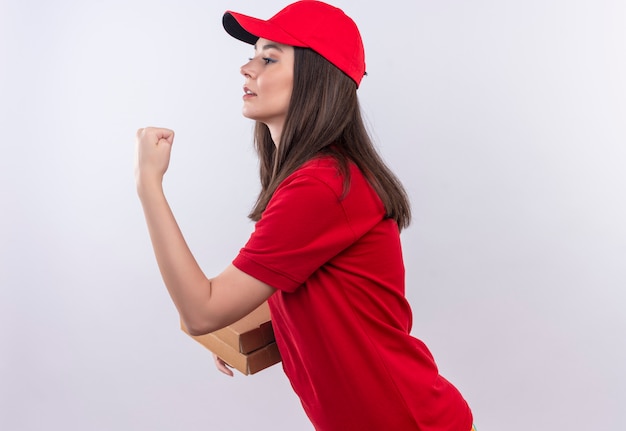 Jeune livreuse portant un t-shirt rouge en bonnet rouge tenant une boîte à pizza et montrant le poing sur fond blanc isolé