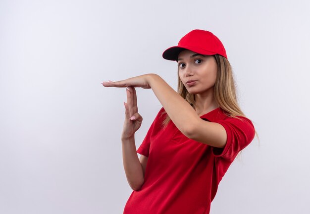 Jeune livreuse portant un uniforme rouge et une casquette montrant le geste de délai d'attente isolé sur un mur blanc