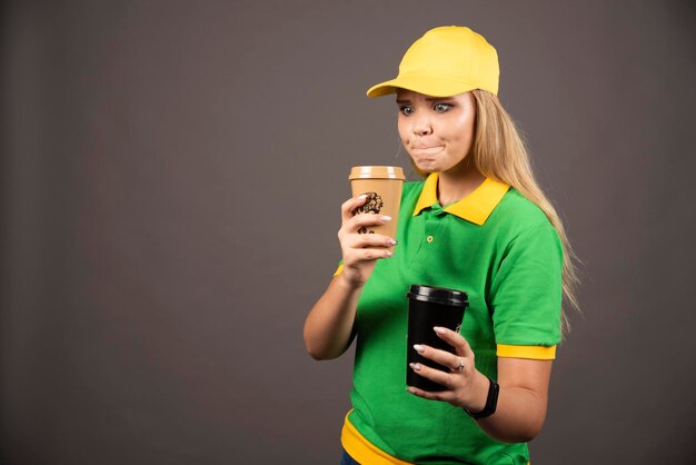 Jeune livreuse tenant des tasses de café sur fond sombre. Photo de haute qualité