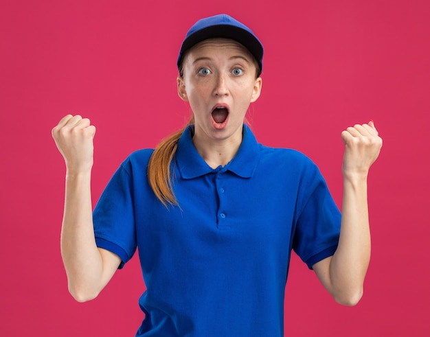 Jeune livreuse en uniforme bleu et casquette étonnée et surprise en serrant les poings