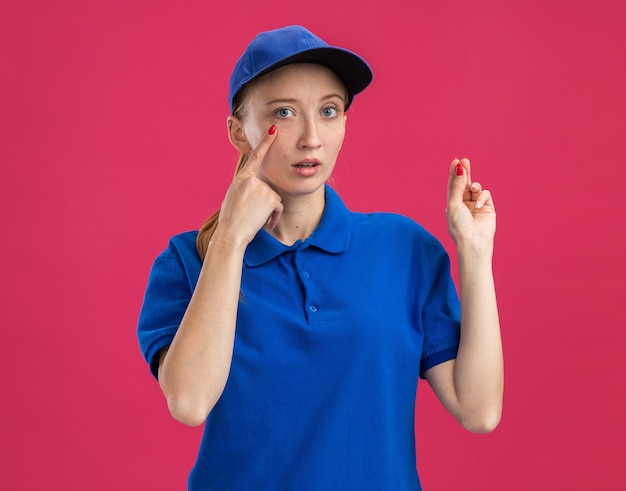 Jeune livreuse en uniforme bleu et casquette surprise en pointant l'index sur son œil