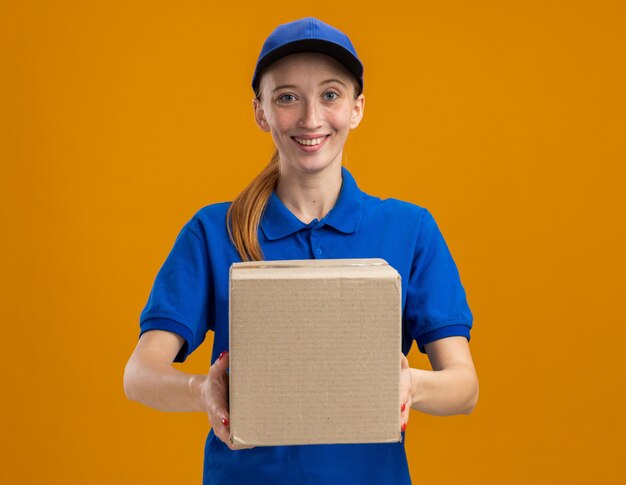 Jeune livreuse en uniforme bleu et casquette tenant une boîte en carton souriante confiante