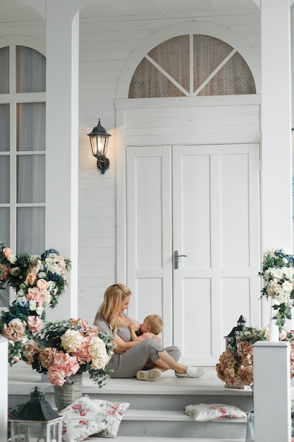 Photo gratuite jeune maman allaiter bébé, assis sur le sol près du porche de la maison en plein air.