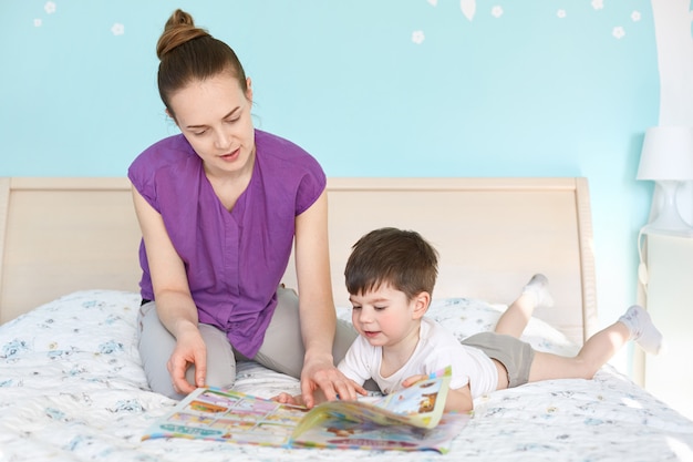Jeune maman attentionnée lit un magazine avec des photos pour les enfants à son petit fils