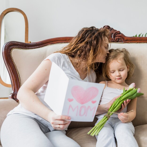 Jeune maman embrassant sa fille tenant la carte de voeux pour la fête des mères