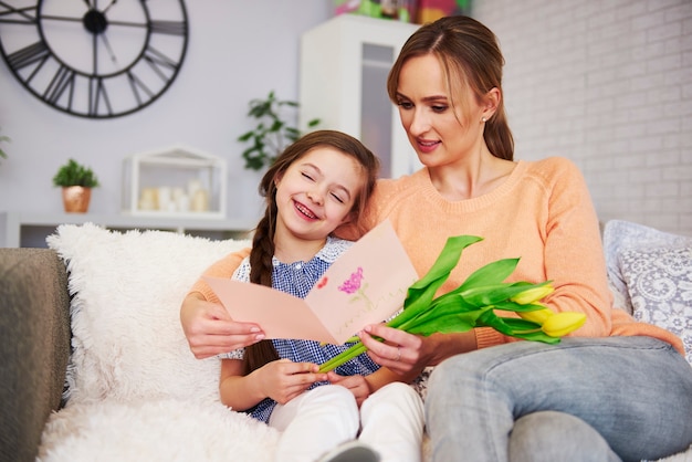 Jeune maman recevant une carte de voeux et une fleur le jour de la fête des mères