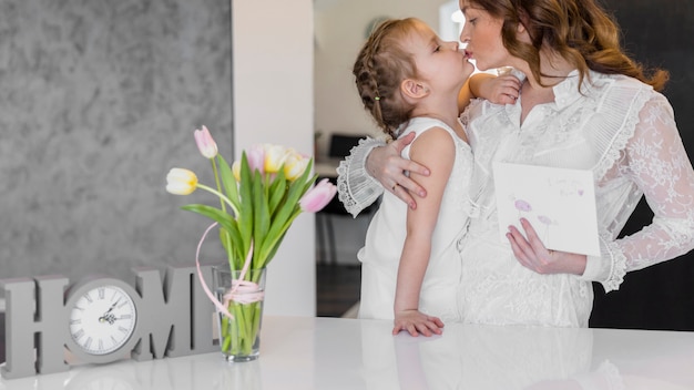 Jeune maman et sa fille s'embrassant à la maison